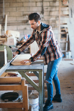 Carpenter sawing a board with a table saw in his workshop.