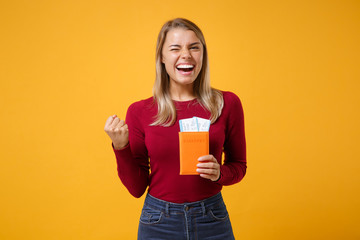 Laughing young blonde woman girl in casual clothes posing isolated on yellow orange wall background. People lifestyle concept. Mock up copy space. Hold passport tickets, doing winner gesture blinking.