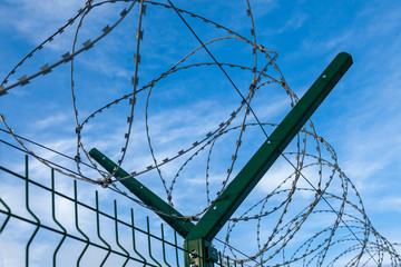 Barbed wire coiled on top of a green metal fence