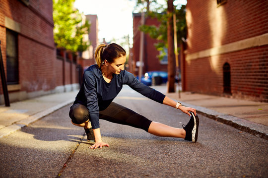 A female runner stretches on a city street.