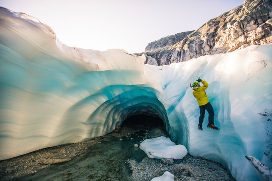 Man ice climbing next to glacial cave.