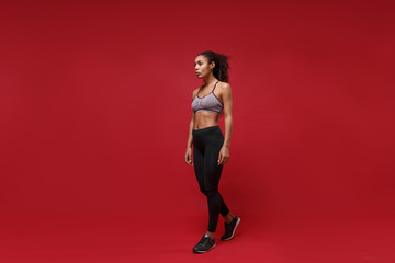 Fototapeta na wymiar Attractive young african american sports fitness woman in sportswear posing working out isolated on red wall background, studio portrait. Sport exercises healthy lifestyle concept. Looking aside.