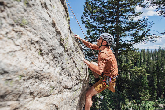 Man holds on to rock with fingertips while climbing with a rope