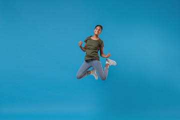 Fototapeta na wymiar Joyful young african american woman girl in casual clothes posing isolated on bright blue wall background studio portrait. People lifestyle concept. Mock up copy space. Jumping, doing winner gesture.