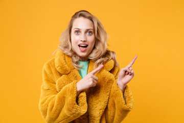 Excited young blonde woman girl in yellow fur coat posing isolated on orange wall background studio...