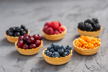 Homemade tartlets from shortcrust pastry with different ripe berries - blueberries, raspberries, blackberries, sea buckthorn, dogwood, chokeberry on a dark background