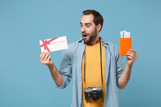 Surprised traveler tourist man in summer clothes with photo camera isolated on blue background. Passenger traveling on weekends. Air flight journey Hold passport boarding pass ticket gift certificate.