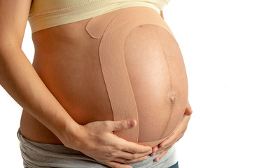 Pregnant woman with therapeutic tape. Back pain in pregnancy, alternative kinesio tape therapy.