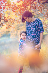 Happy family. Pregnant mom and little daughter hugging and kissing at sunset in autumn in forest. Laughter, happiness and fun together