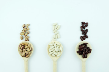 Different varieties of beans white, red and Pinto, lie on wooden spoons on a white background. Copy...