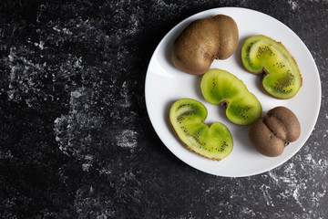 Ugly fruits and vegetables, ugly kiwi berries on a white plate, flat lay.