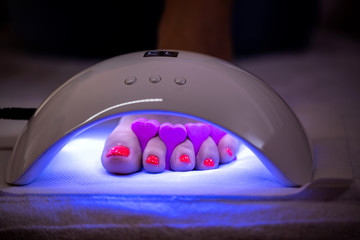 Red toenail polisher curing in a ultra violet led nail lamp