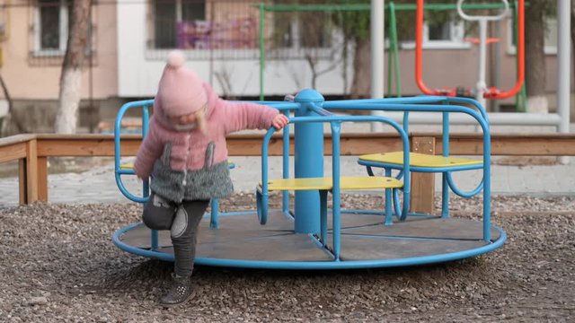 Lonely little kid girl gets off a carousel at children's playground