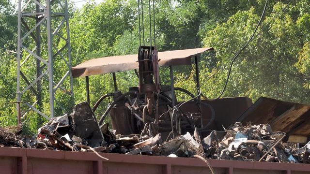 4k video of big crane with electric magnet lifting metal scrap and loading it in high pressure recycling machine on the scrapyard