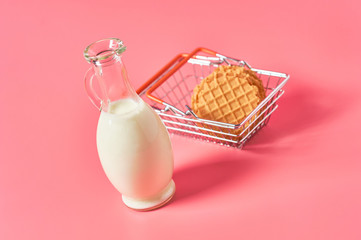 Full jug of fresh milk, yogurt or kefir near thin waffles in market basket on pink background