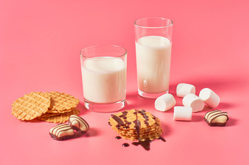 Two full glasses of fresh milk, yogurt or kefir near thin waffles, chocolate candies, marshmallow...