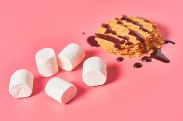 Sweet thin waffles with chocolate cream near marshmallow on pink background