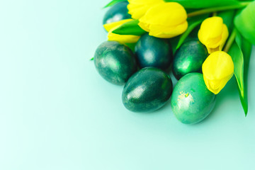 Beautiful spring concept with Easter eggs and yellow tulips on turquiose green background. Copy space. Close-up.