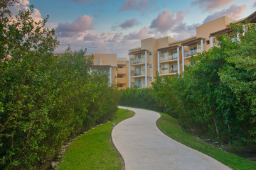 A yellow stucco resort hotel beyond a walking trail and shrubs