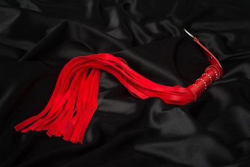 Red whip on a black silk background. Accessories for adult sexual games