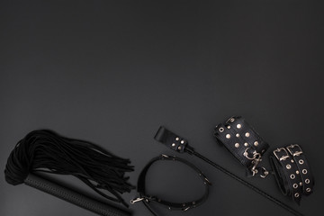 Leather handcuffs, black whip, collar and stack on black background