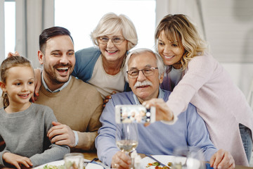 Fototapeta na wymiar Happy multi-generation family having fun while taking selfie in dining room.