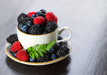 Tea cup with berries closeup on a wooden table. Raspberry, blackberry, bilberry in a cup. Summer berry mix. Copy space.