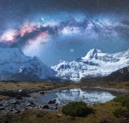 Milky Way over snowy mountains and lake at night. Landscape with snow covered high rocks and starry sky reflected in water in Nepal. Sky with stars. Fantastic view with bright milky way in Himalayas