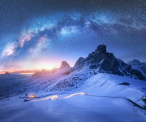 Milky Way over snowy mountains and blurred car headlights on the winding road at night in winter....