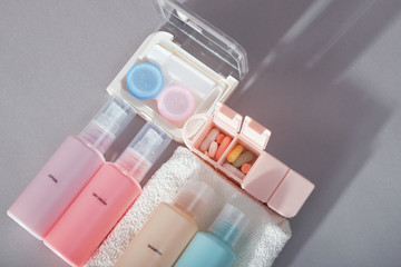 Travel kit. Set of four small plastic bottles for cosmetic products, kit for contact lenses, pill organizer, towel. Gray background with shadows.