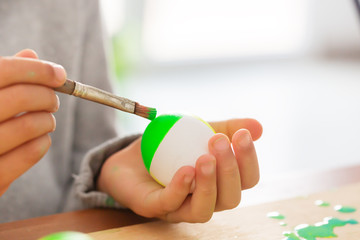 Boy in his room paints easter eggs with a brush