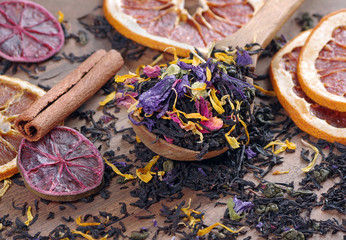blended tea. black tea with dry flower petals and citrus fruits. dry black tea leaves in a wooden...