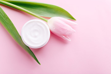Jar of cream and pink tulip on pink background, top view. Professional cosmetic products