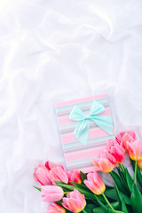 Gift box and bouquet of pink tulips on white bed.