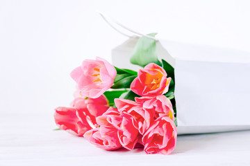 Fresh pink tulip flowers in paper bag on wooden table.