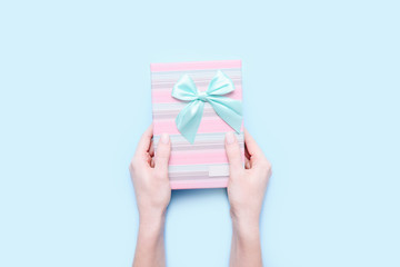 Woman's hands with a gift box on blue background. Top view