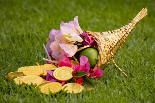Cuerno de la abundancia con flores, monedas de oro, dulces y fruta sobre un campo verde saturado