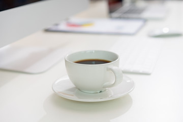 A cup of coffee and office supplies on the white desk