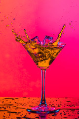 Droplets of Drink Spilling Out of The High Glass Goblet with Ice Cubes and Colorful Liquid. Isolated On Colorful Background.