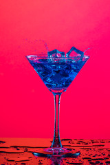 Droplets of Drink Spilling Out of The Glass Goblet with Icecubes and Colorful Liquid. Isolated Over Colorful Background.