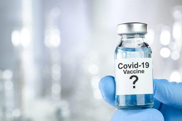 Possible cure concept with a hand in blue medical gloves holding Coronavirus, Covid 19 virus, vaccine vial