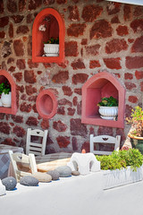 Traditional and Empty Home Restaurant with Chairs and Dining Tables in Oia or Ia Village at Santorini Island in Greece Against Decorated Paved Wall.