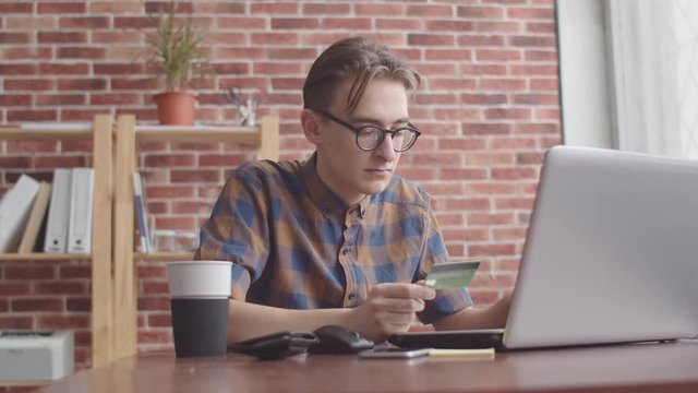 The guy enters the Bank card data into the laptop. A hipster prints a credit card number in a laptop for online purchases. Student with a nose piercing makes online purchases