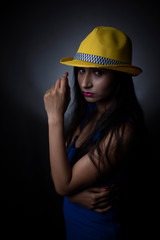 Fashion portrait of an young and attractive Indian Bengali brunette girl in blue western dress and yellow cap in front of a black studio background. Indian fashion portrait and lifestyle.