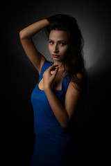 Naklejka premium Fashion portrait of an young and attractive Indian Bengali brunette girl with blue western dress in front of a black studio background. Indian fashion portrait and lifestyle.
