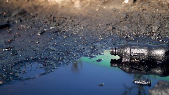 4k dolly video of plastic bottle lying in black oil or diesel waste pubble on the ground. Concept of ecology disaster and industrial damage to nature