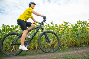 Beautiful girl cyclist rides a field with sunflowers on a bicycle. Healthy lifestyle and sport. Leisure and hobbies