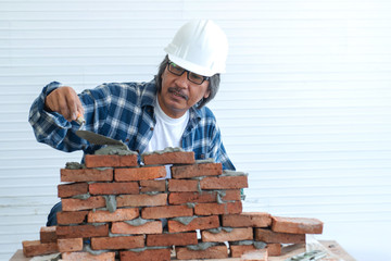 Happy Asian senior worker in hardhat with trowel installing brick masonry