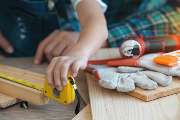 Close-up of boy hands measuring wooden plank with measuring tape, education concept