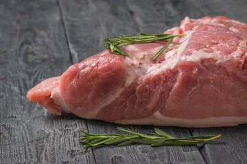A large piece of pork and two sprigs of rosemary on a wooden table.